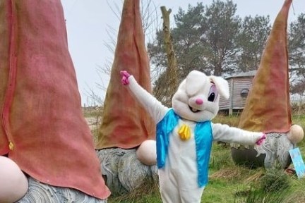 Person in bunny costume posing with large gnome statues in a grassy area.