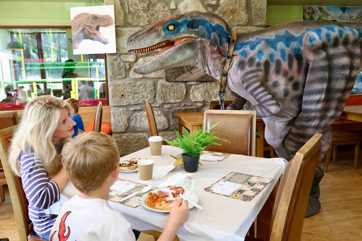 A dinosaur interacts with a family at a dining table indoors.