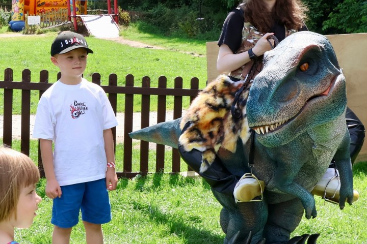 Person in a dinosaur costume with kids in a park.