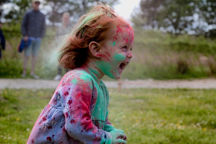 Child covered in colorful powders laughing outdoors.