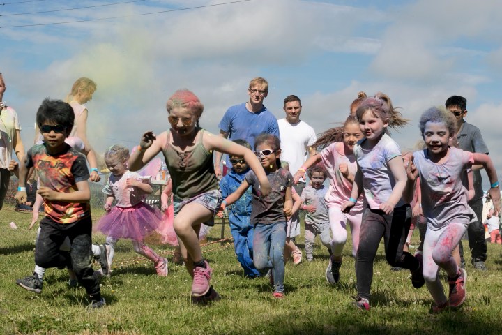 Children covered in colored powder running outdoors during a festival.