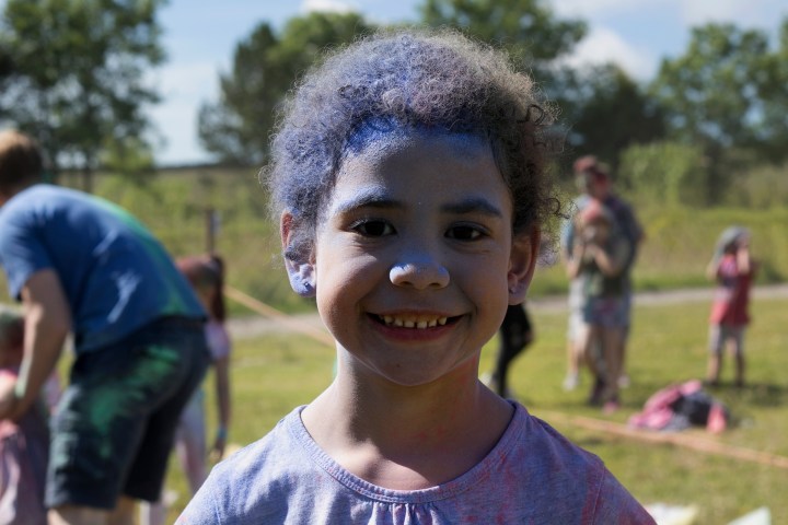Smiling child with blue face paint outdoors at a park event.