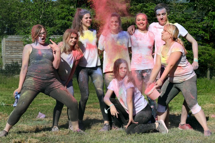 Group of people outdoors covered in colorful powder, smiling and posing energetically.